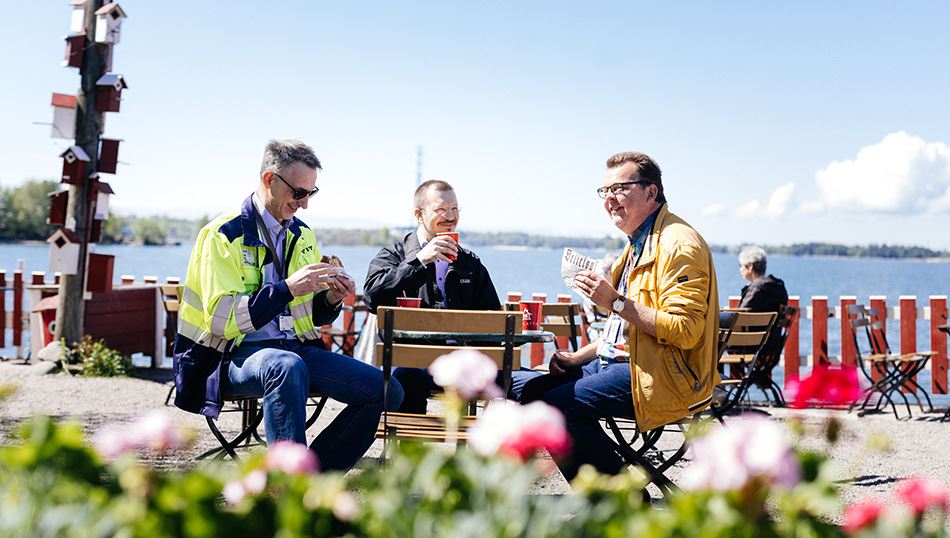 YIT:n suunnittelujohtaja Matti Varstala, Espoon kaupungin hankepäällikkö Markus Salin sekä YIT:n Tiistilän rakenteilla olevan puurakenteisen koulu- ja päiväkotikiinteistön työmaapäällikkö Harry Mäkinen hyväntuulisina yhdessä kahvilla Regatalla Helsingissä aurinkoisena päivänä meren pilkottaessa taustalla.